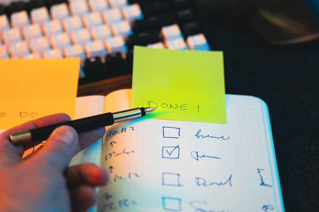 Close-up of hand holding pen over notebook checklist with sticky notes labeled 'DONE!'